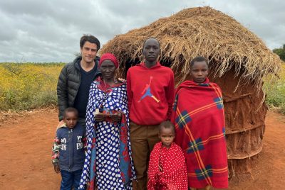 A group of people stand in front of a grass-roofed hut. 