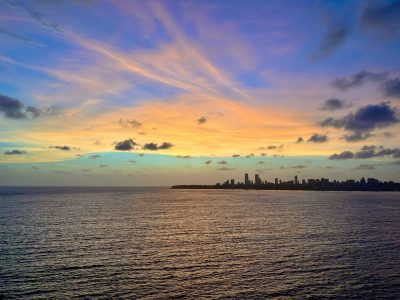 A city skyline can be seen across a large body of water with a yellow sunset behind